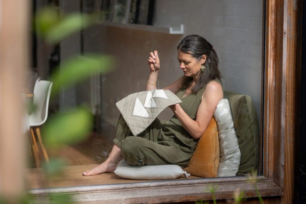Woman sitting in a window sewing patchwork