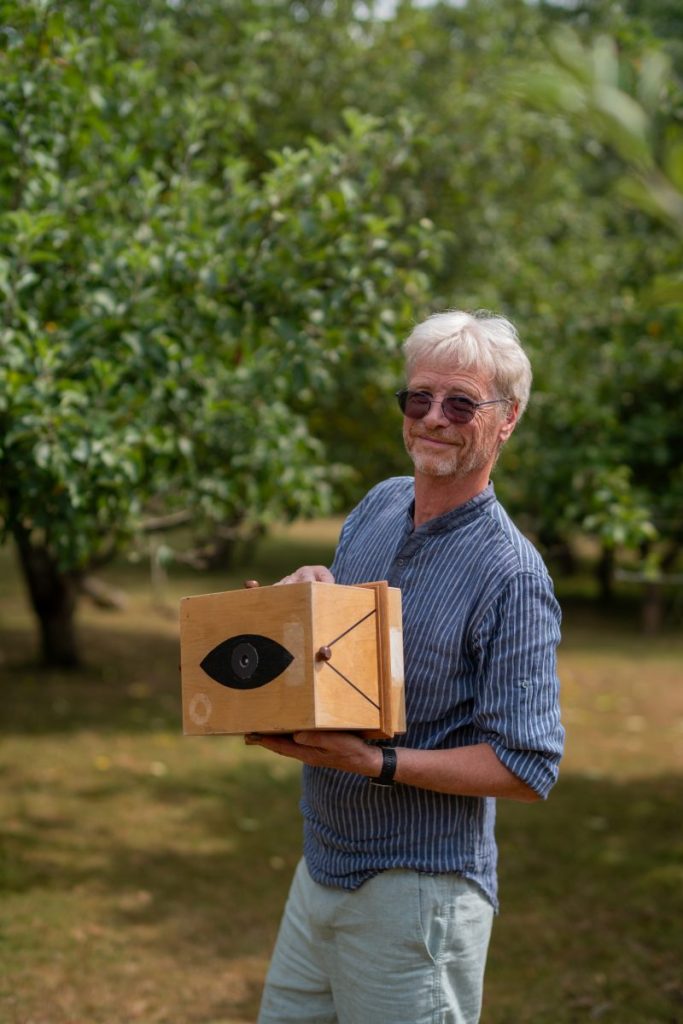 Alasdair Gordon standing in a field holding a pinhole camera.
Photo: Jim Wileman